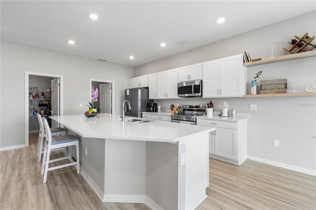 kitchen with stainless steel appliances, open shelves, light wood-style flooring, a large island with sink, and white cabinets