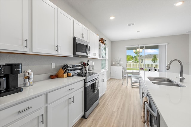 kitchen with appliances with stainless steel finishes, a sink, a chandelier, light wood finished floors, and white cabinets