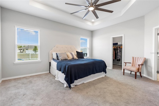 bedroom featuring a raised ceiling, carpet floors, a walk in closet, baseboards, and recessed lighting