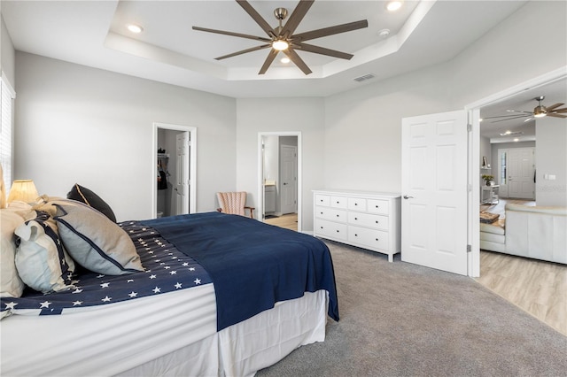 bedroom featuring a raised ceiling, light colored carpet, recessed lighting, ensuite bathroom, and a spacious closet