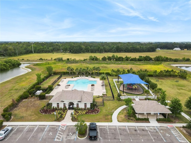 drone / aerial view of a nearby body of water, a pool area, and a tree filled landscape