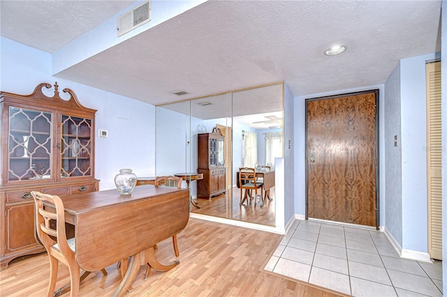 dining space with a textured ceiling, visible vents, baseboards, and light wood-type flooring