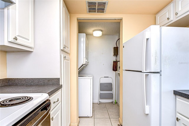 kitchen featuring light tile patterned floors, freestanding refrigerator, stacked washing maching and dryer, white cabinetry, and visible vents