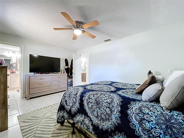 bedroom featuring a ceiling fan, a textured ceiling, marble finish floor, ensuite bath, and visible vents