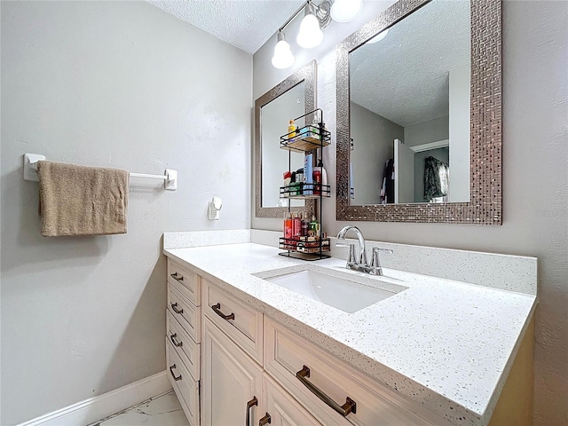 bathroom with vanity, a textured ceiling, baseboards, and marble finish floor