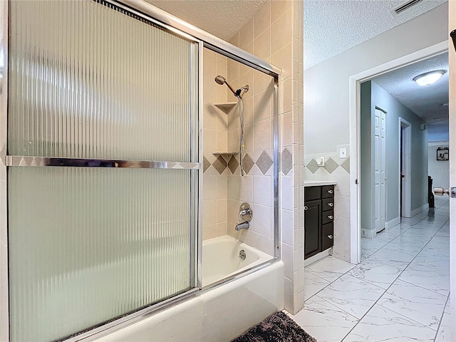 bathroom with tile walls, marble finish floor, a textured ceiling, visible vents, and shower / bath combination with glass door