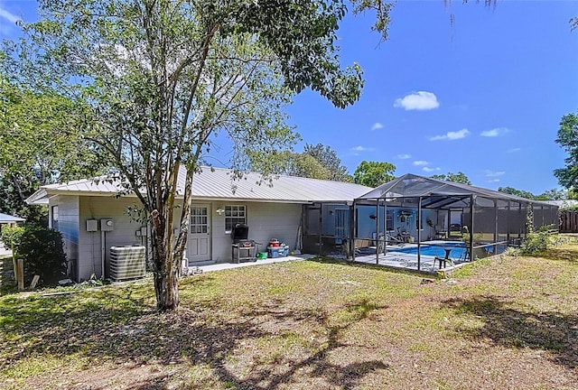 rear view of house featuring a patio area, an outdoor pool, concrete block siding, a lawn, and central AC unit