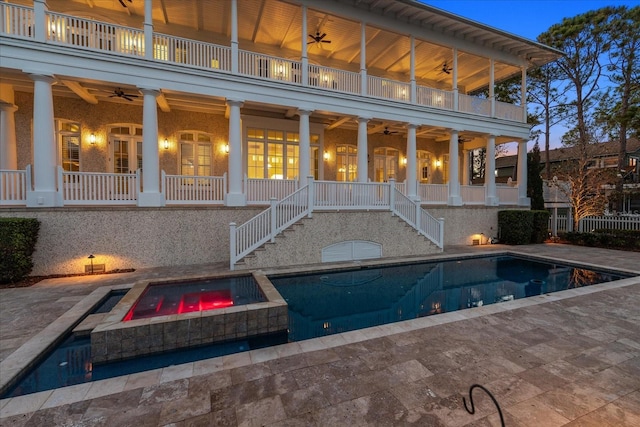 back of property with a ceiling fan, stairs, an in ground hot tub, and a balcony