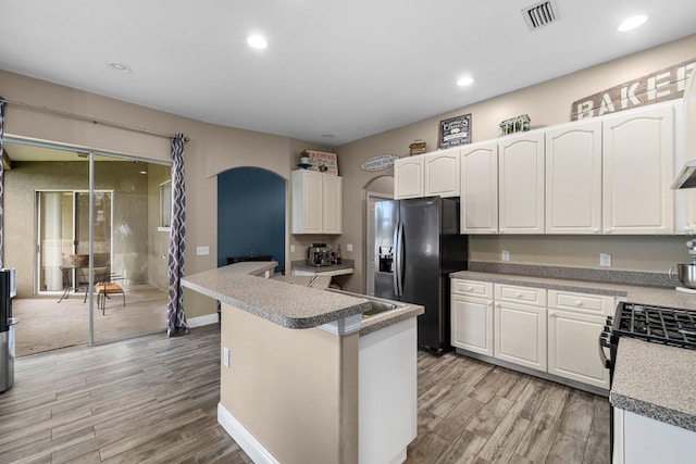 kitchen with light wood-type flooring, visible vents, arched walkways, white cabinets, and fridge with ice dispenser