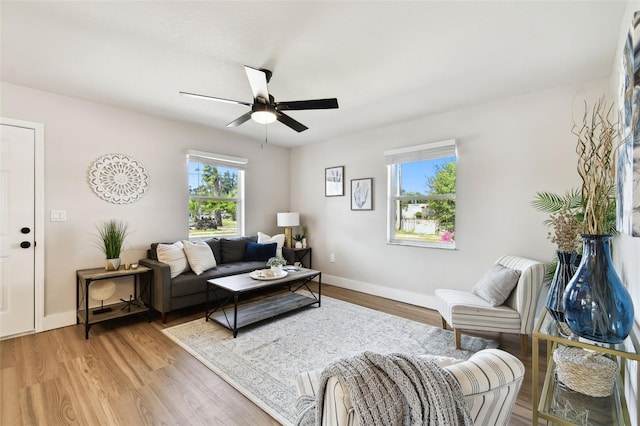 living room featuring ceiling fan, baseboards, and light wood-style flooring