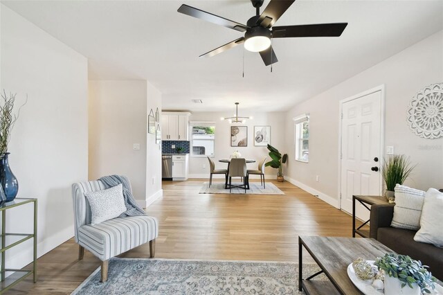 living room featuring light wood-type flooring, ceiling fan, baseboards, and a chandelier