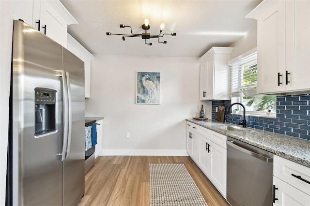 kitchen with appliances with stainless steel finishes, a sink, baseboards, a chandelier, and backsplash