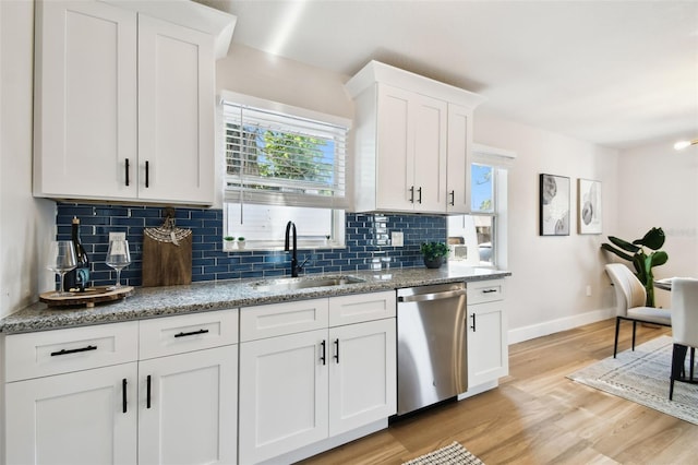 kitchen with stainless steel dishwasher, a sink, baseboards, light wood finished floors, and backsplash