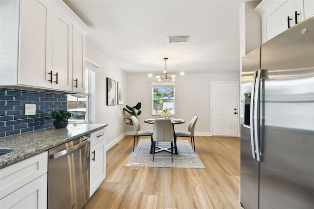 kitchen with stainless steel appliances, backsplash, light wood-style flooring, a chandelier, and baseboards