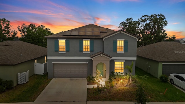 traditional-style home featuring an attached garage, roof mounted solar panels, stucco siding, fence, and driveway