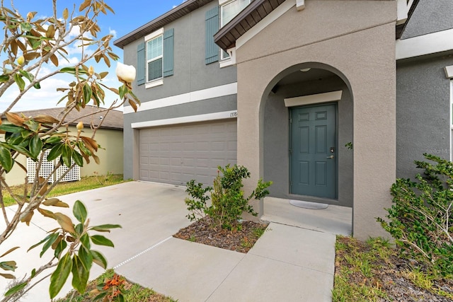entrance to property with stucco siding, driveway, and a garage
