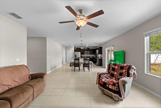 living room with light tile patterned floors, visible vents, baseboards, and ceiling fan