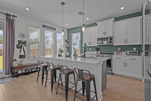 kitchen with stainless steel appliances, a sink, white cabinetry, light countertops, and a kitchen island with sink
