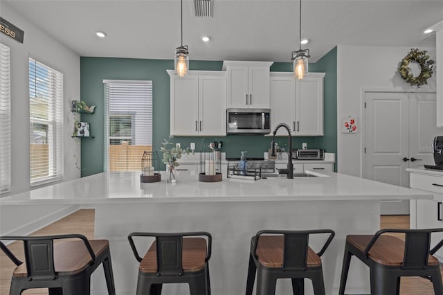 kitchen with stainless steel microwave, a breakfast bar, visible vents, a center island with sink, and white cabinets