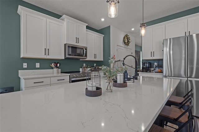 kitchen with hanging light fixtures, appliances with stainless steel finishes, a kitchen bar, and white cabinetry