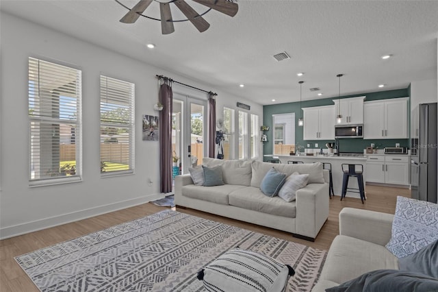 living room featuring light wood-type flooring, visible vents, recessed lighting, ceiling fan, and baseboards