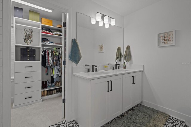 full bath with baseboards, a spacious closet, double vanity, and a sink