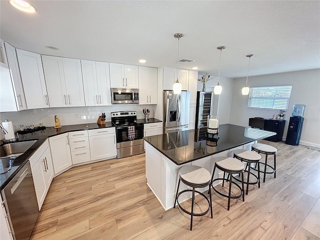 4715 W Chapin Ave, Tampa, FL 33611 - kitchen featuring appliances with stainless steel finishes, light wood-type flooring, a sink, a breakfast bar area, and white cabinetry