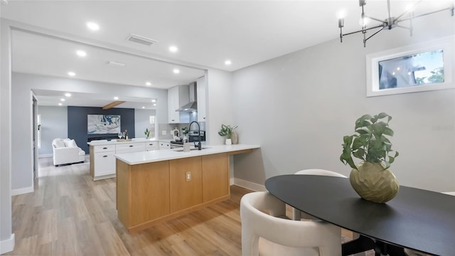 1715 N Alexander Rd, Tampa, FL 33603 - kitchen featuring a peninsula, light wood-style floors, wall chimney range hood, light countertops, and a chandelier