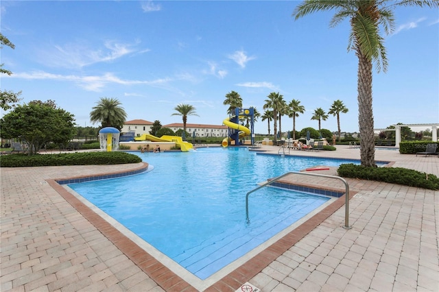 community pool with a water play area, a patio area, a water slide, and playground community