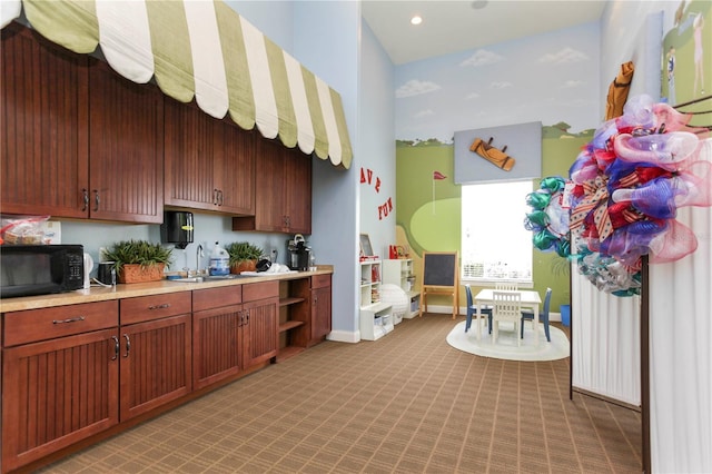 kitchen with a sink, baseboards, light countertops, light carpet, and black microwave