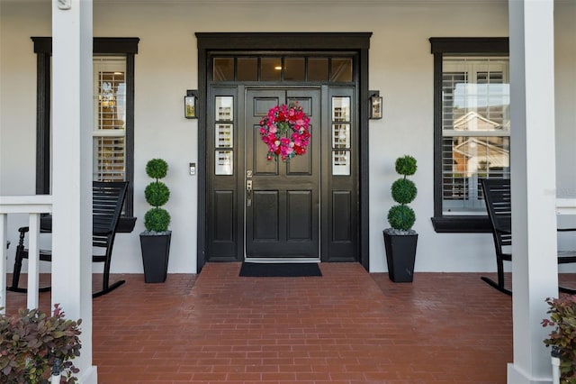view of exterior entry with stucco siding and a porch