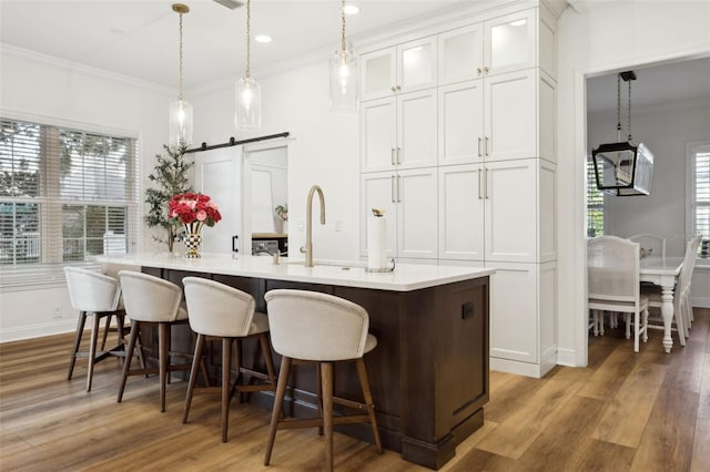 kitchen featuring ornamental molding, a barn door, white cabinets, wood finished floors, and a kitchen breakfast bar