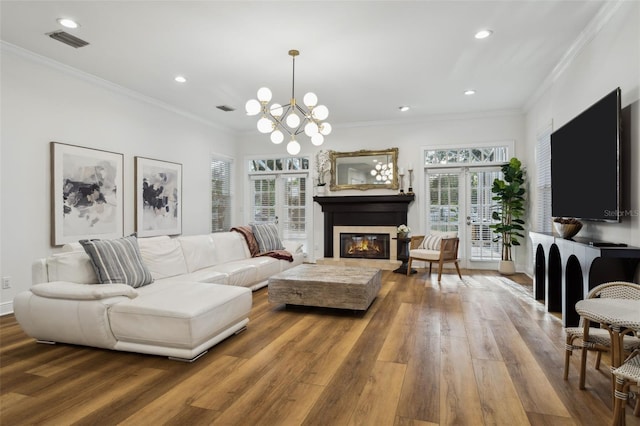 living area with wood finished floors, a glass covered fireplace, a chandelier, recessed lighting, and ornamental molding