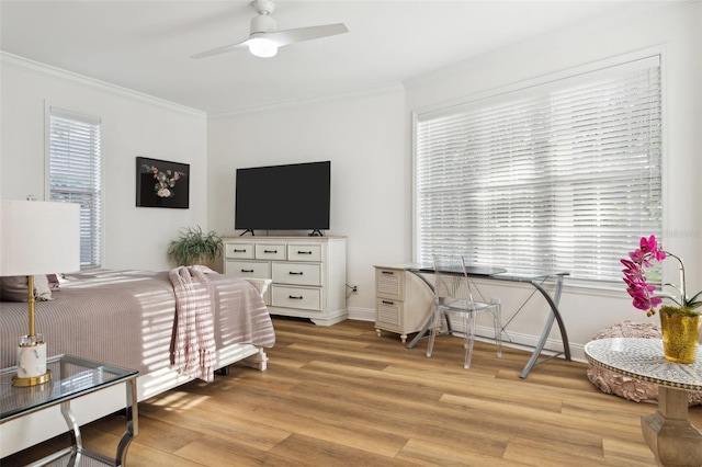 bedroom featuring light wood-type flooring, ornamental molding, multiple windows, and a ceiling fan