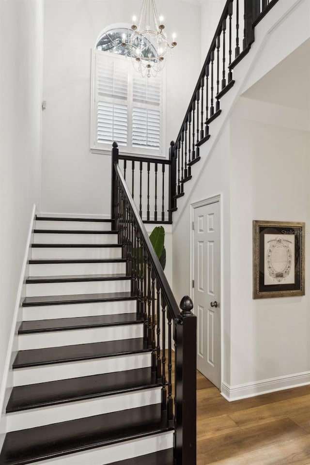 staircase with baseboards, wood finished floors, a chandelier, and a high ceiling