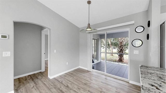 2675 Cherokee St, North Port, FL 34286 - unfurnished dining area with vaulted ceiling, light wood-style floors, arched walkways, and baseboards