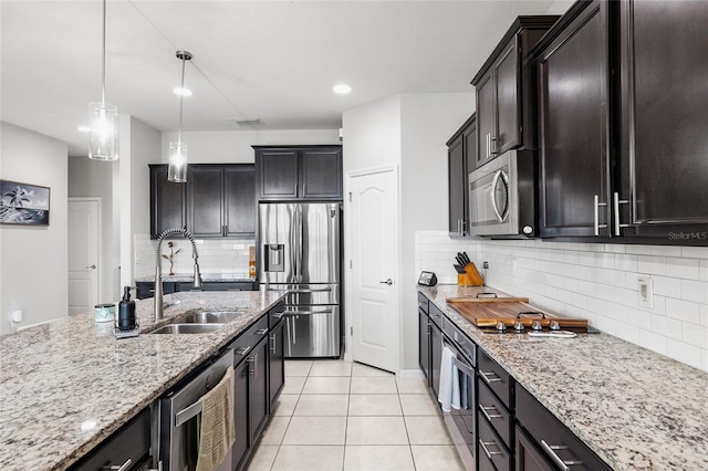 kitchen featuring light stone countertops, pendant lighting, a sink, decorative backsplash, and appliances with stainless steel finishes