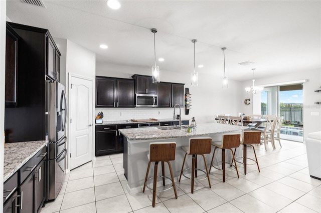 kitchen with a breakfast bar area, a sink, stainless steel appliances, backsplash, and light stone counters