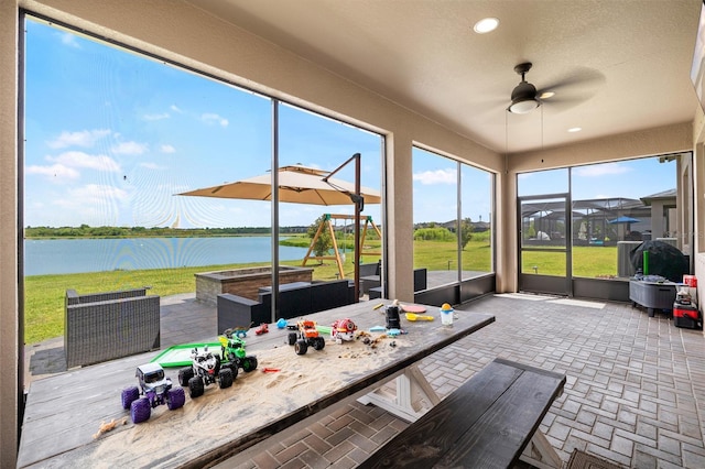 sunroom featuring ceiling fan, a water view, and outdoor dining space