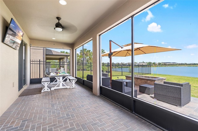 sunroom / solarium featuring a water view, brick patterned floor, and a ceiling fan