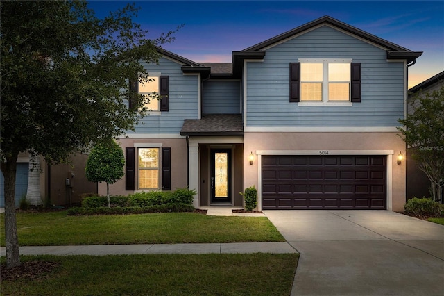 traditional home featuring a lawn, driveway, a garage, stucco siding, and roof with shingles
