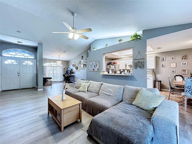 living room with ceiling fan with notable chandelier, light wood-type flooring, visible vents, a textured ceiling, and vaulted ceiling