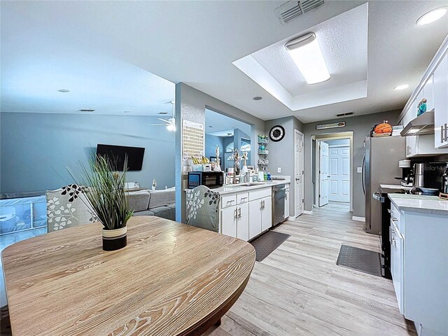 kitchen with stainless steel dishwasher, visible vents, a raised ceiling, light countertops, and white cabinets