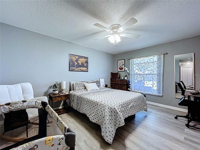 bedroom featuring baseboards, a textured ceiling, light wood-style floors, and a ceiling fan