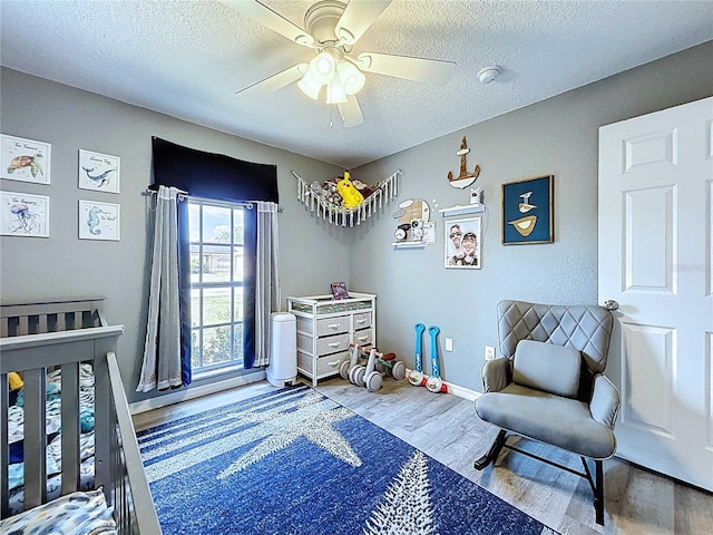 bedroom featuring baseboards, ceiling fan, a textured ceiling, and wood finished floors