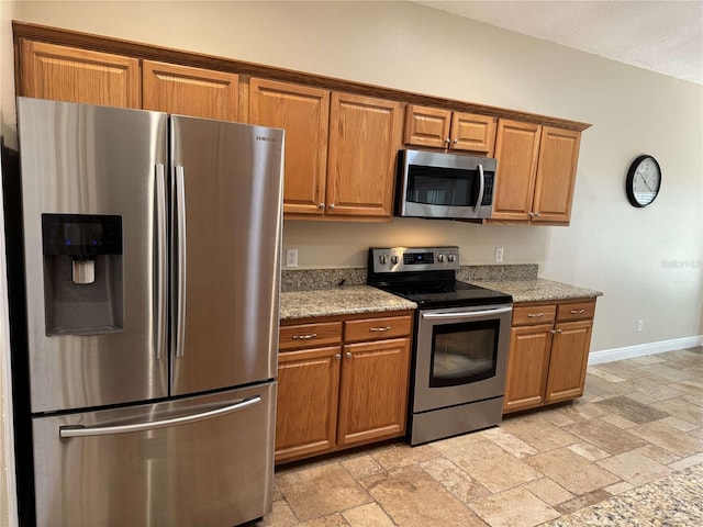 1608 Fox Glen Ct, Winter Springs, FL 32708 - kitchen featuring stone tile floors, brown cabinetry, baseboards, light stone counters, and stainless steel appliances
