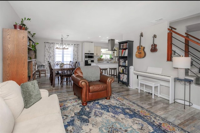 living room featuring wood finished floors, visible vents, baseboards, stairway, and a chandelier