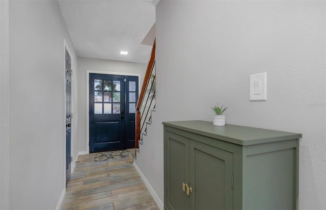 doorway with baseboards, stairs, and light wood-style floors