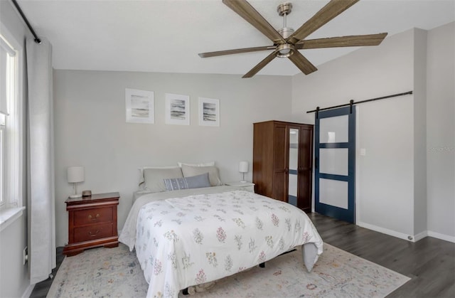bedroom featuring ceiling fan, a barn door, baseboards, and wood finished floors