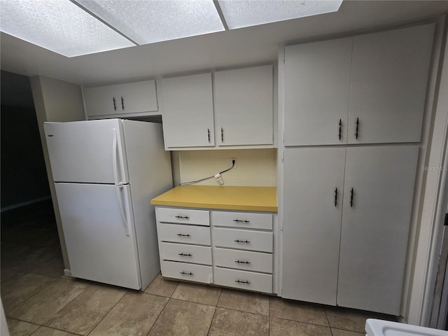 kitchen featuring freestanding refrigerator, light tile patterned flooring, light countertops, and white cabinets